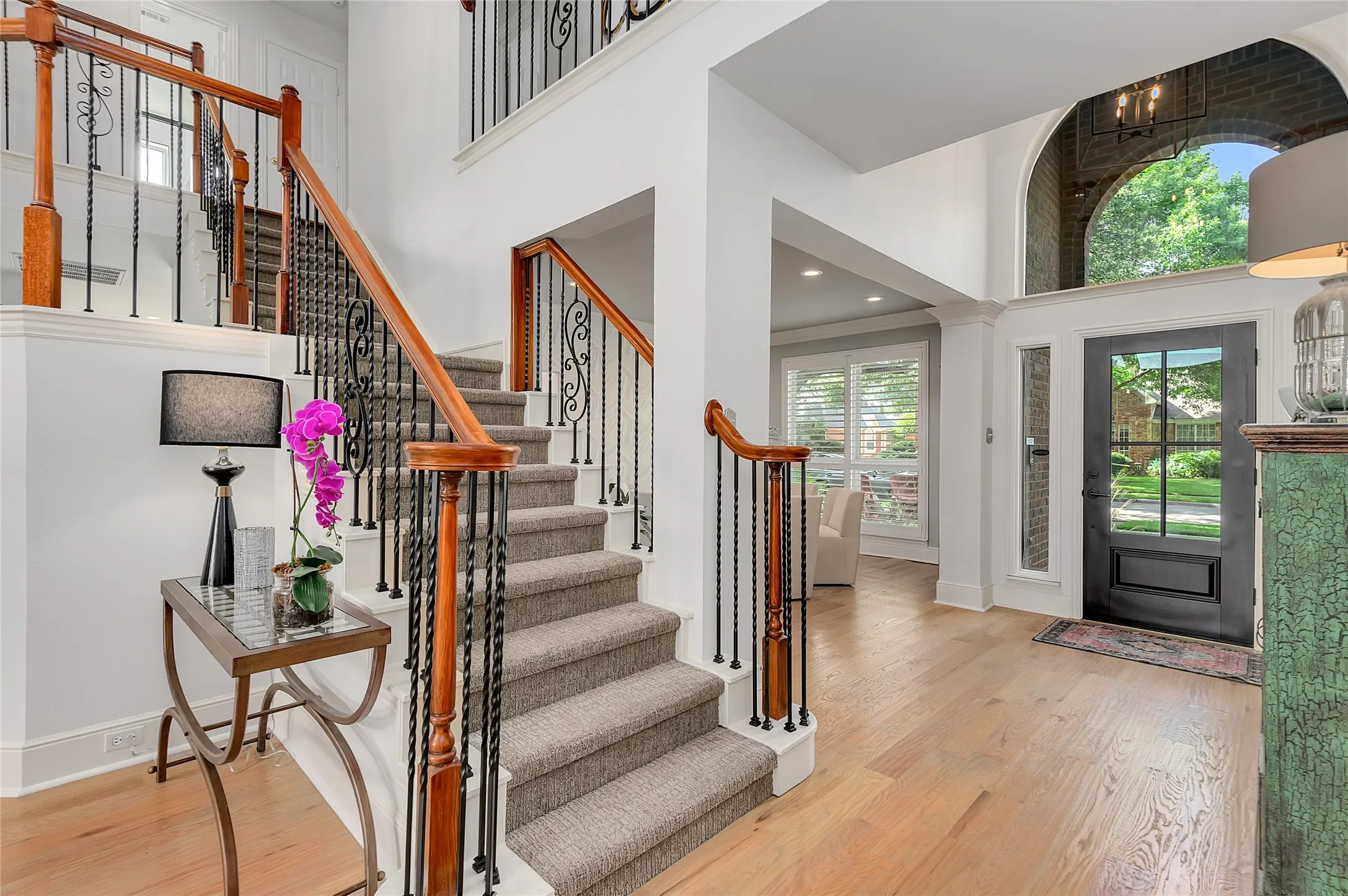 Two-story foyer featuring hardwood flooring and a carpeted staircase with wrought iron balusters and wood handrails