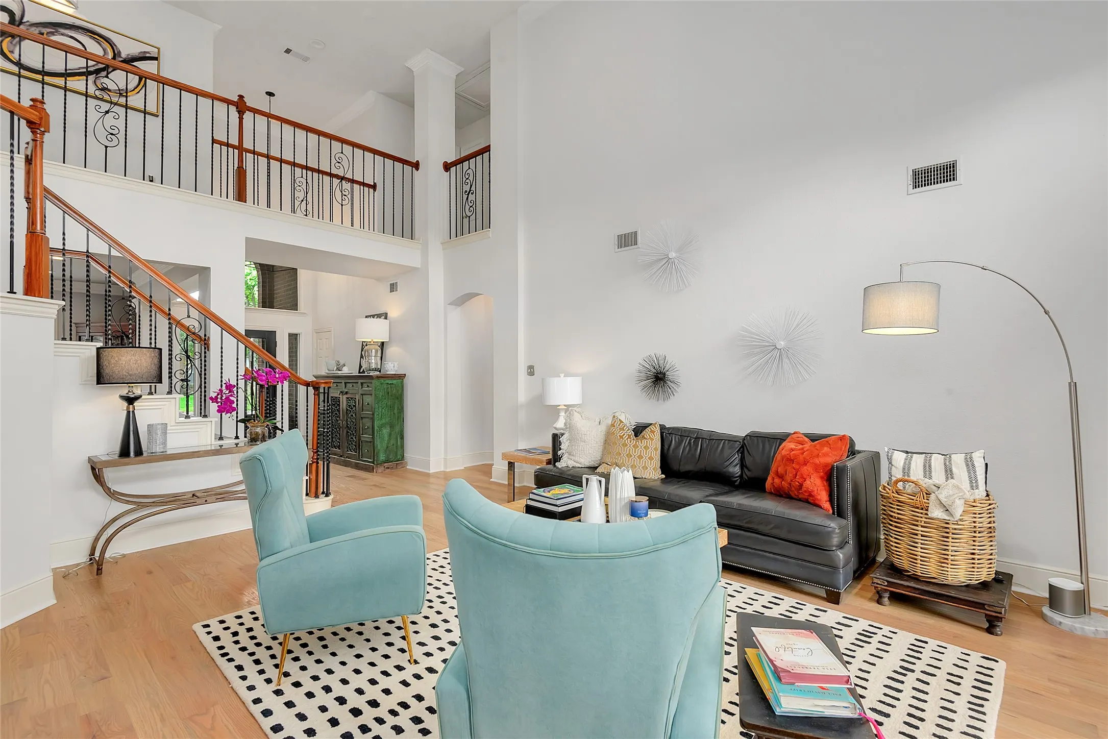 Two-story living area featuring wood-finish flooring, a grand staircase with wrought iron and wood railing, and an open-concept upper-level walkway