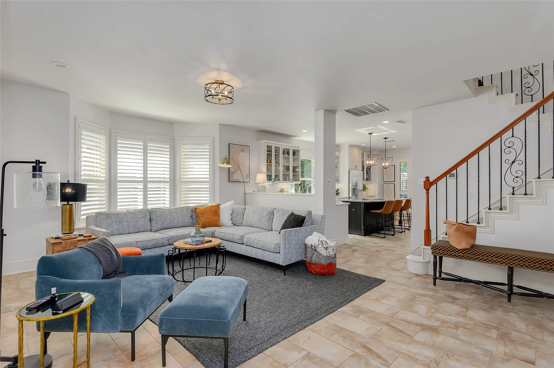 Open-concept living space featuring wood-finish flooring, a prominent staircase with wrought iron balusters and wood handrail, and a kitchen island with seating