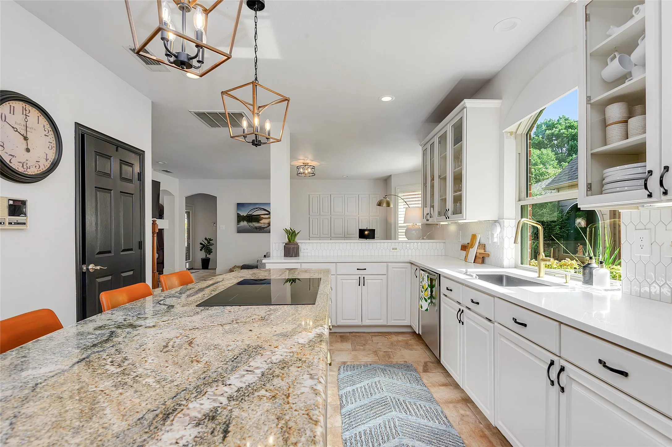 Contemporary kitchen featuring an expansive island with a built-in cooktop, white shaker cabinetry, and a gold-finish faucet