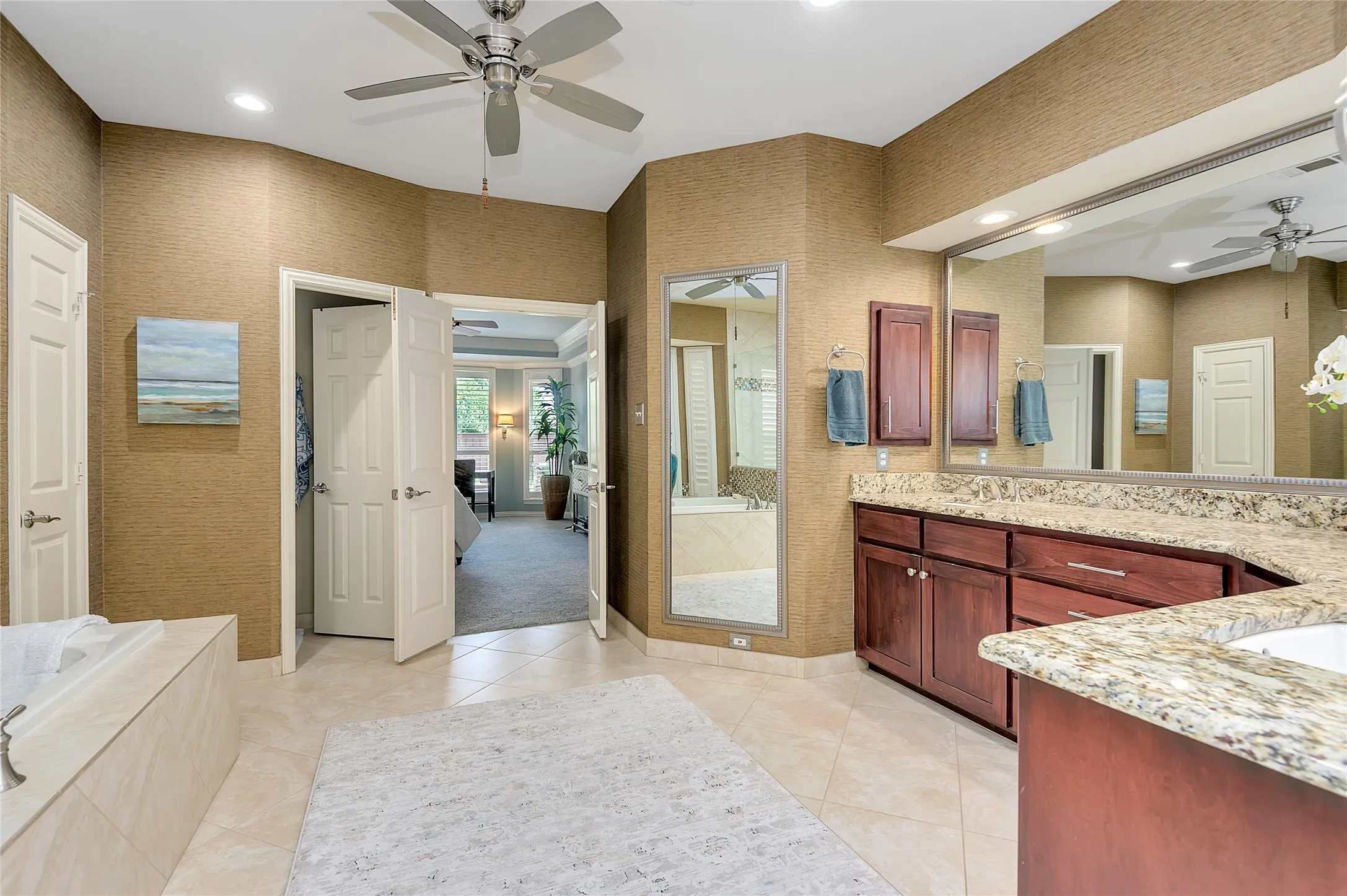 Spacious bath with dual ceiling fans, tile flooring, rich wood cabinetry, ample counter space, and a built-in soaking tub