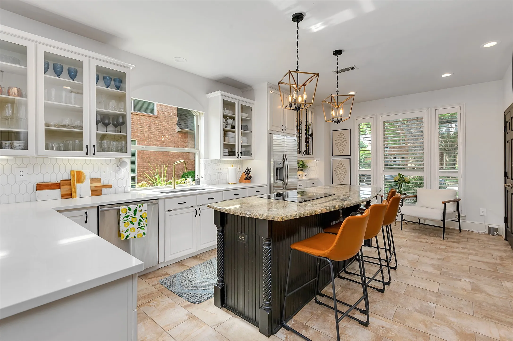 Spacious kitchen featuring an island with a built-in cooktop, light-toned countertops, white cabinetry with glass-front uppers, stainless steel appliances, and a tiled backsplash