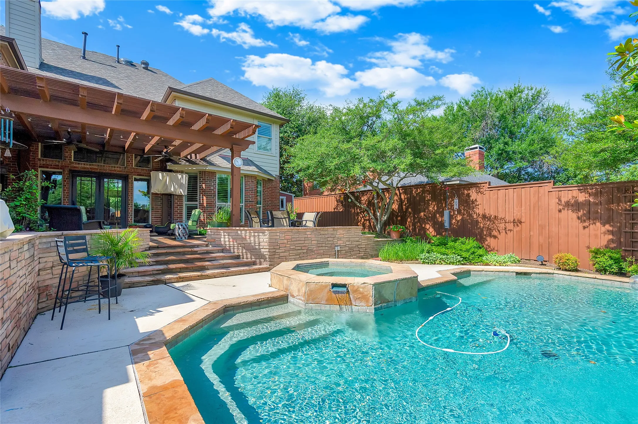 Expansive backyard featuring a custom pool with integrated spa, a tiered stone patio, and a covered pergola with ceiling fans