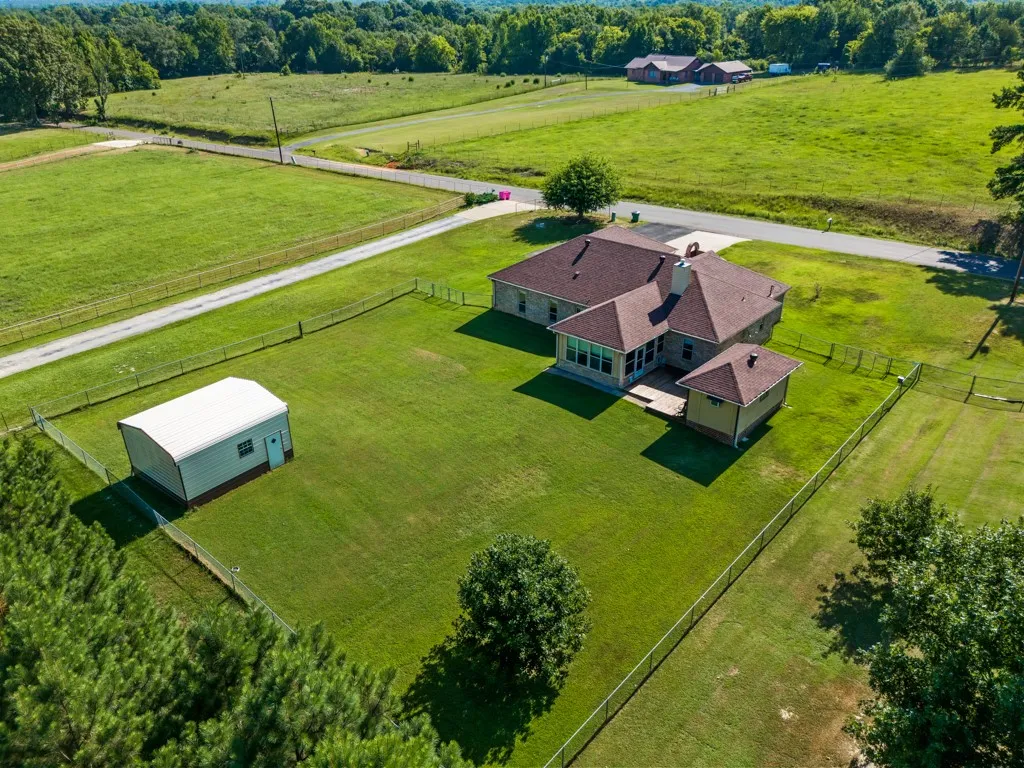 Expansive property featuring a stone-clad residence with a sunroom, a detached utility building, and a fenced yard