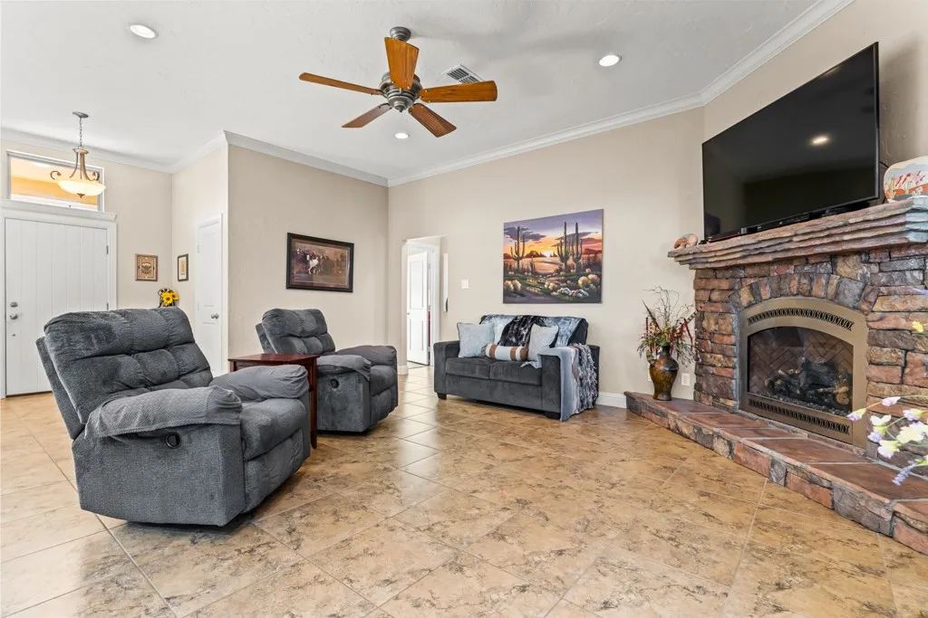 Spacious living area featuring tile flooring, a prominent stone-clad fireplace with a hearth, crown molding, and recessed lighting