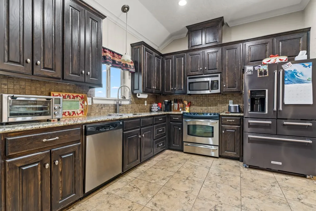 Kitchen featuring dark wood cabinetry, stainless steel appliances, speckled countertops, and a tiled backsplash