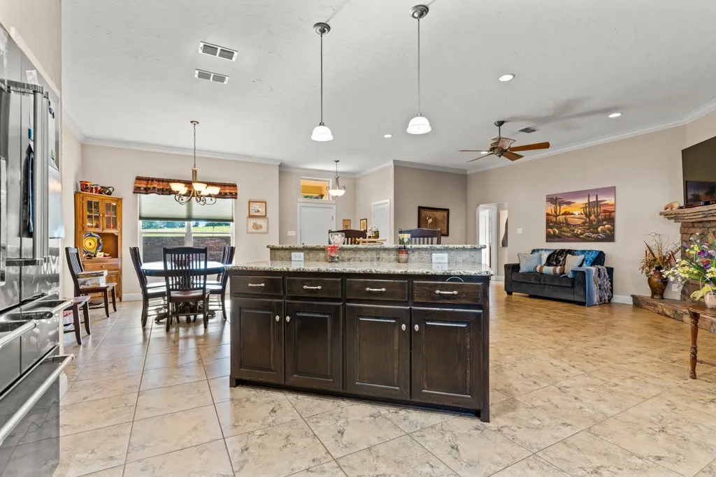 Expansive open-concept space featuring a large kitchen island with dark wood cabinetry and granite countertops, tile flooring, recessed lighting, and crown molding