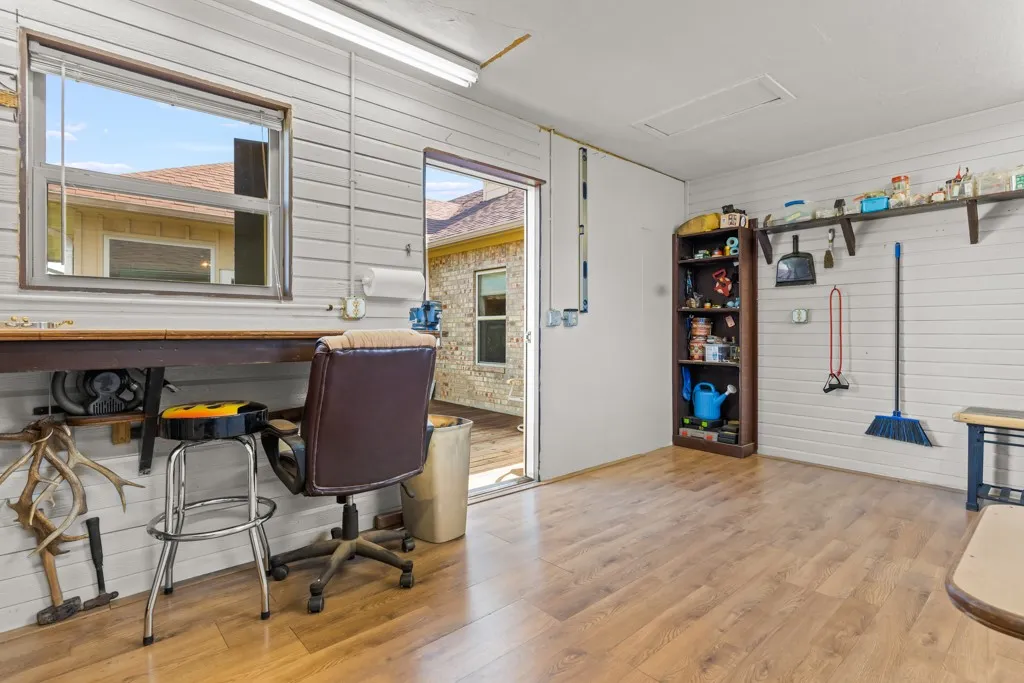 Versatile interior space featuring wood-finish flooring, a built-in workbench, an overhead fluorescent light fixture, and an exterior door providing outdoor access