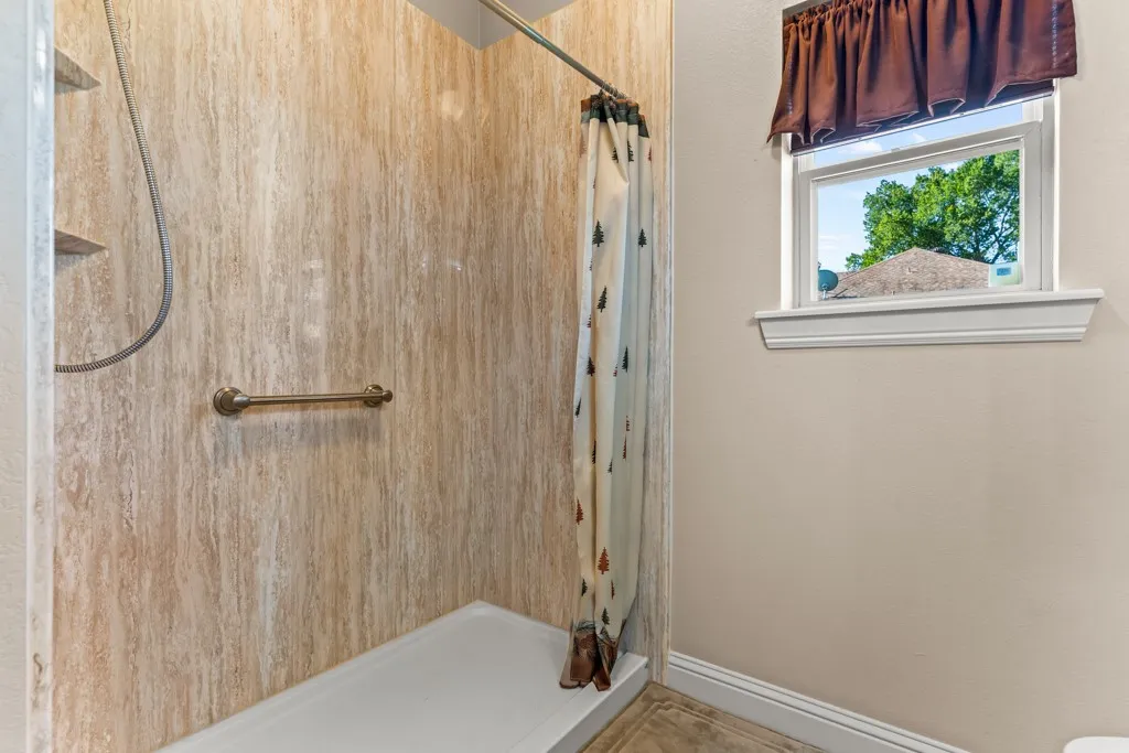 Shower stall featuring textured wall panels, a built-in shelf, and a grab bar