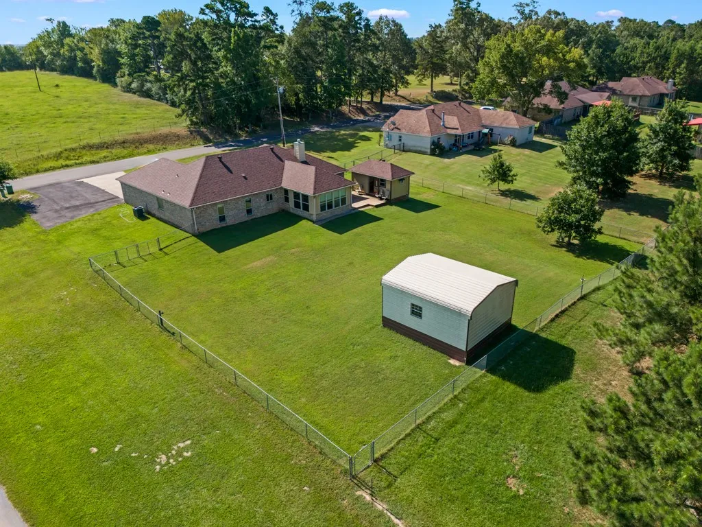 Expansive green grounds featuring a brick exterior single-story residence with a brown shingle roof, a detached metal storage building, and a fenced yard