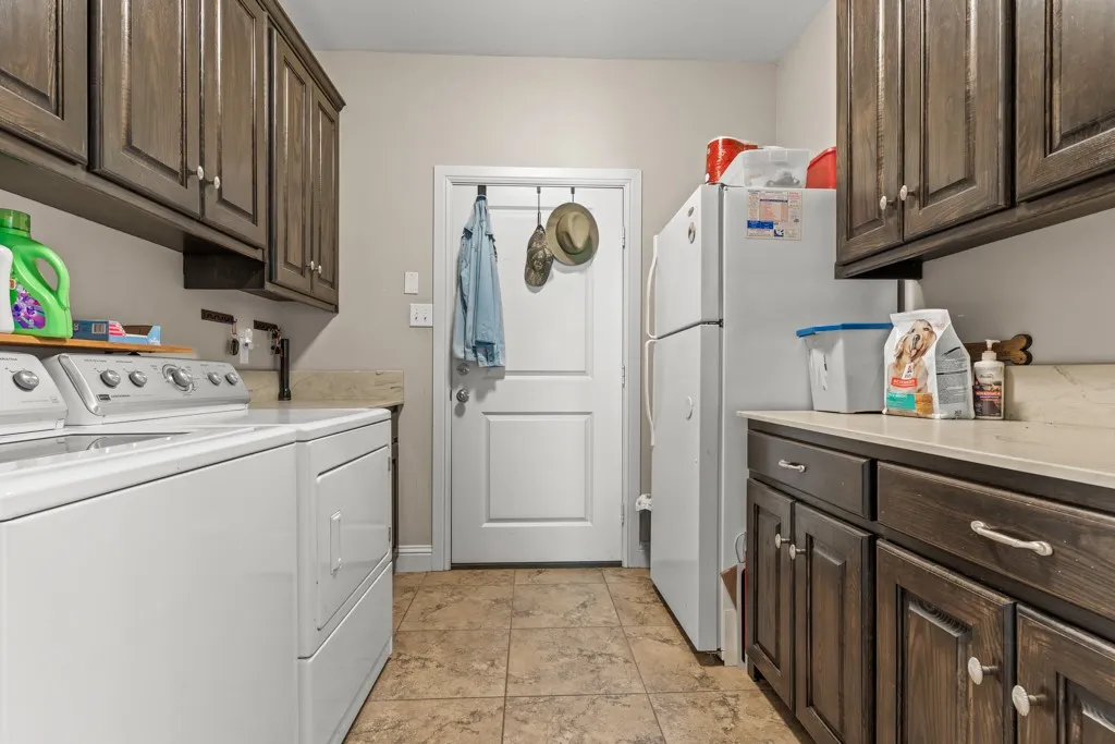 Laundry room featuring a light-toned tile floor, dark wood-finish cabinetry, light-toned countertops, and a white interior door with an over-the-door hook rack
