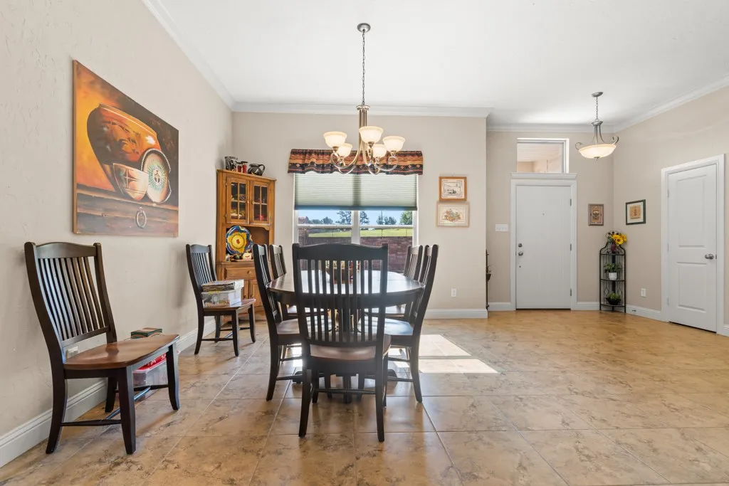 Open-concept dining area featuring tile flooring, crown molding, a multi-light chandelier, and a front entry door with transom window