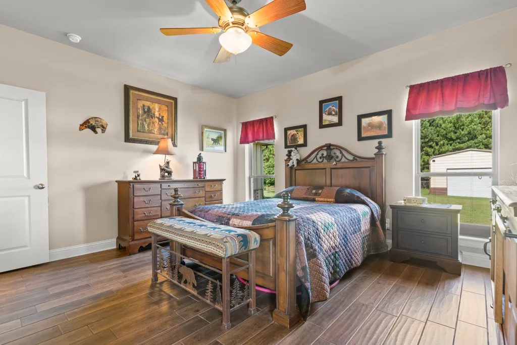 Spacious bedroom with wood-finish flooring, two large windows, a ceiling fan, and light-toned walls