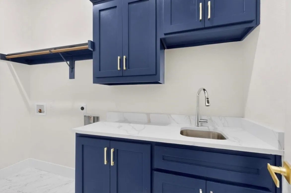 Laundry area featuring custom blue cabinetry, a stainless steel sink with a chrome faucet, white countertops, and a built-in shelving unit