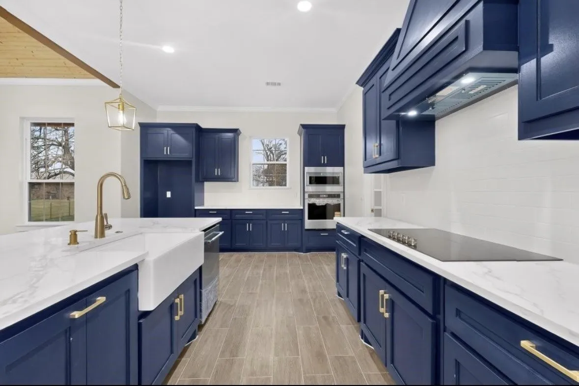 Kitchen featuring blue cabinetry, white countertops, wood-finish flooring, a farmhouse sink with a brass-finish faucet, and a built-in cooktop with a coordinating range hood