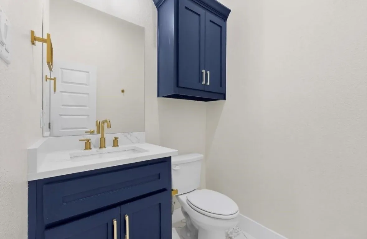 Bathroom featuring a navy blue vanity with gold hardware, a white countertop, and a matching navy blue wall cabinet