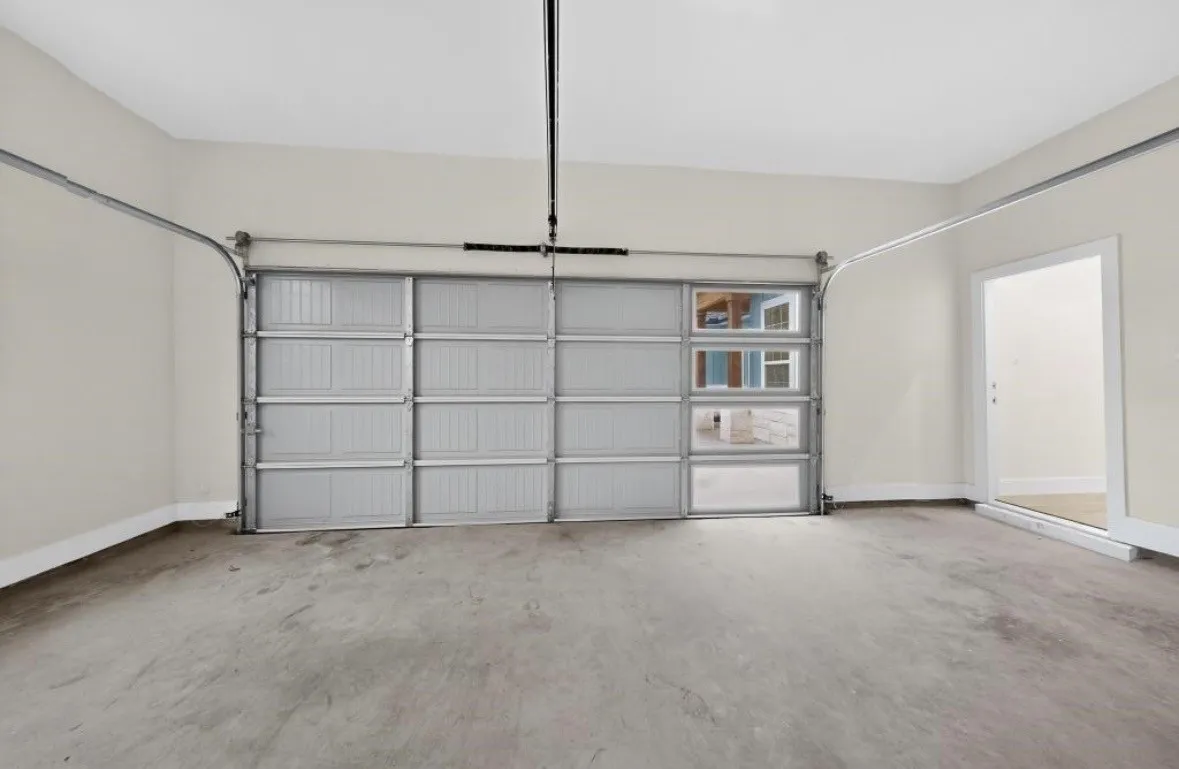 Spacious garage featuring a concrete floor, light neutral walls, and an overhead garage door with frosted window panels