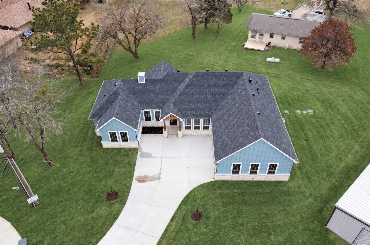 New construction residence featuring a large asphalt shingle roof, light blue vertical siding, and a stone facade foundation