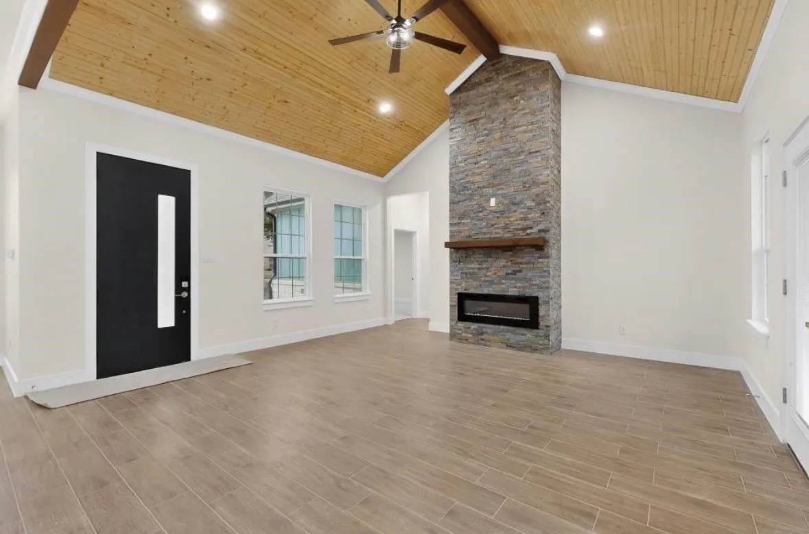 Spacious interior featuring a vaulted wood-plank ceiling, wood-finish flooring, and a stone-clad fireplace with an electric insert