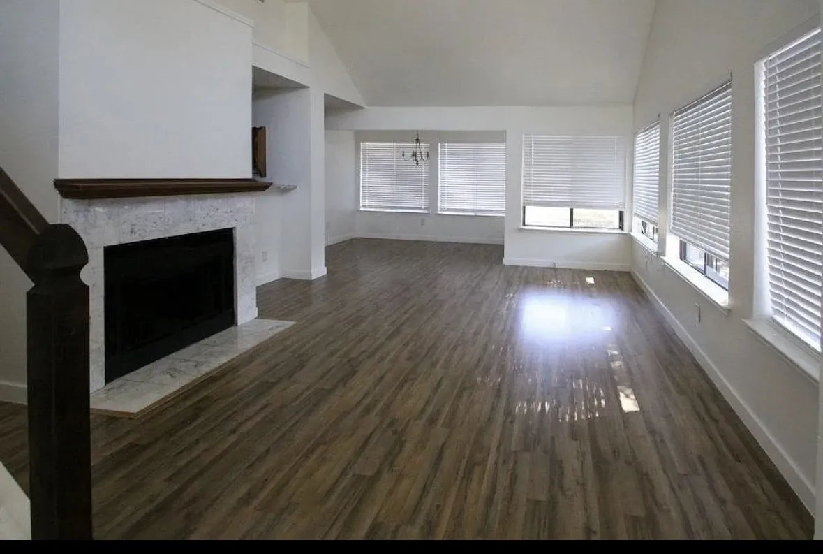 Unfurnished living room featuring lofted ceiling, a fireplace with flush hearth, dark wood-style floors, and a chandelier