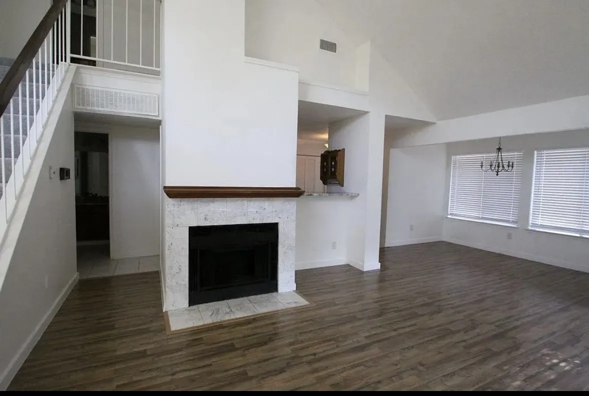Unfurnished living room featuring high vaulted ceiling, a chandelier, stairs, wood finished floors, and a fireplace with flush hearth