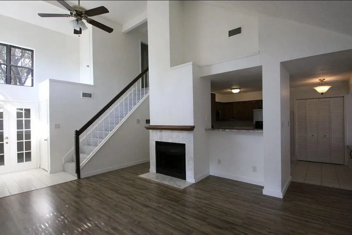 Unfurnished living room with high vaulted ceiling, stairs, wood finished floors, a ceiling fan, and a fireplace with flush hearth