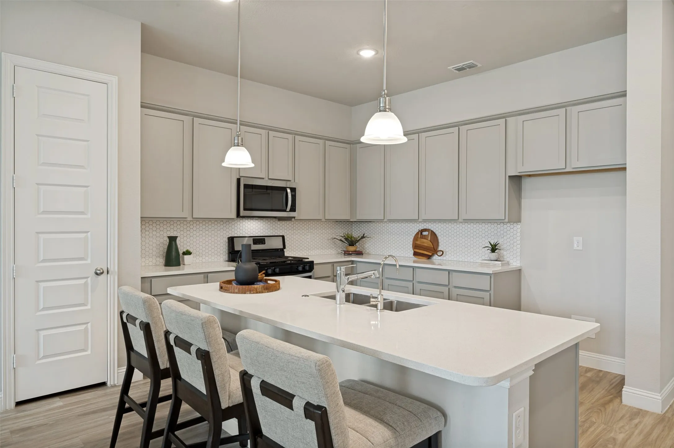 The beautifully appointed kitchen serves as the centerpiece of the home, showcasing an oversized quartz island with bar seating, stainless steel appliances, gas range, designer cabinetry, and stylish pendant lighting. The open-concept design offers effortless flow for entertaining and everyday living