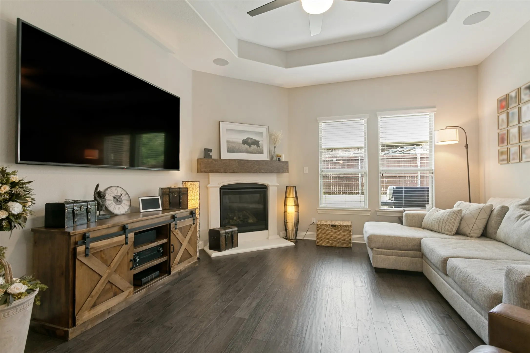 Living area featuring dark wood-finish flooring, a white mantel fireplace with a dark wood beam, and two large windows with blinds