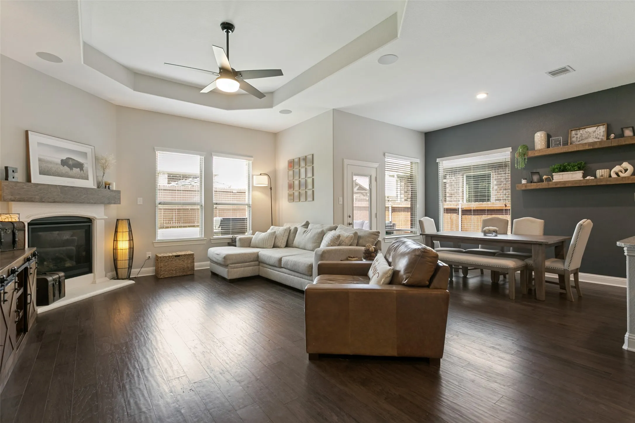 Spacious open-concept living area featuring wood-finish flooring, a tray ceiling with a modern ceiling fan, and recessed lighting