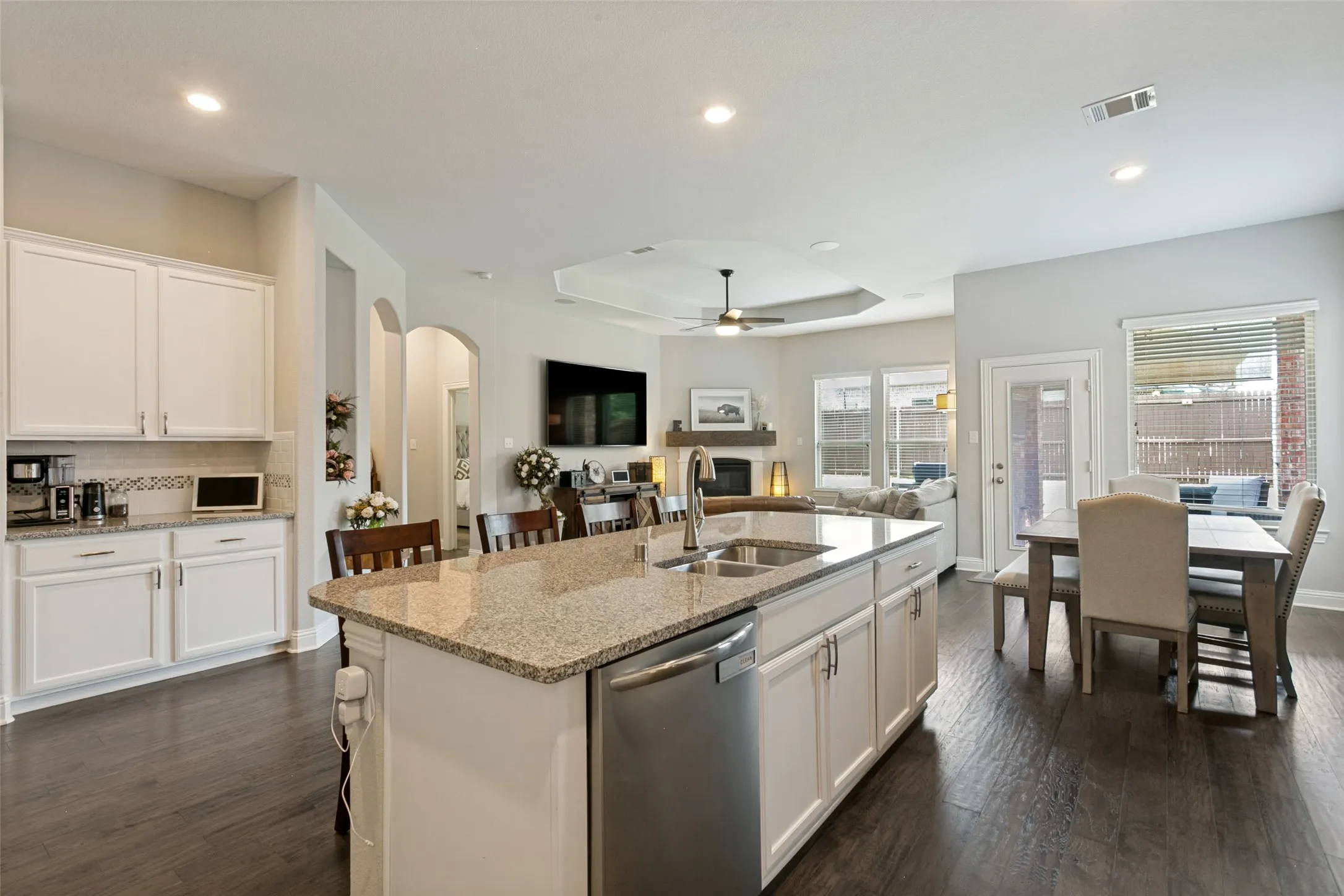 Open-concept kitchen featuring an island with granite countertops, stainless steel appliances, white cabinetry, and wood-finish flooring