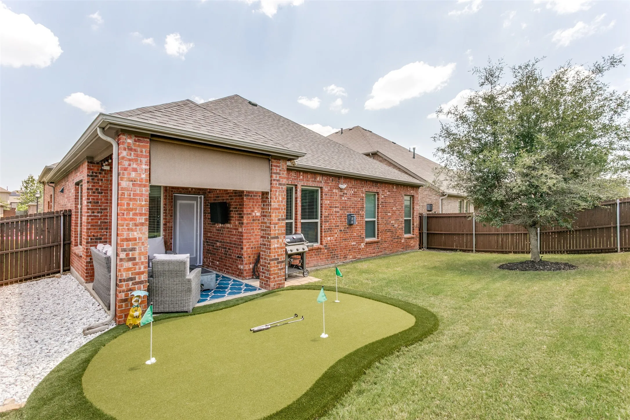 Brick exterior featuring a covered patio with a retractable shade and an outdoor putting green
