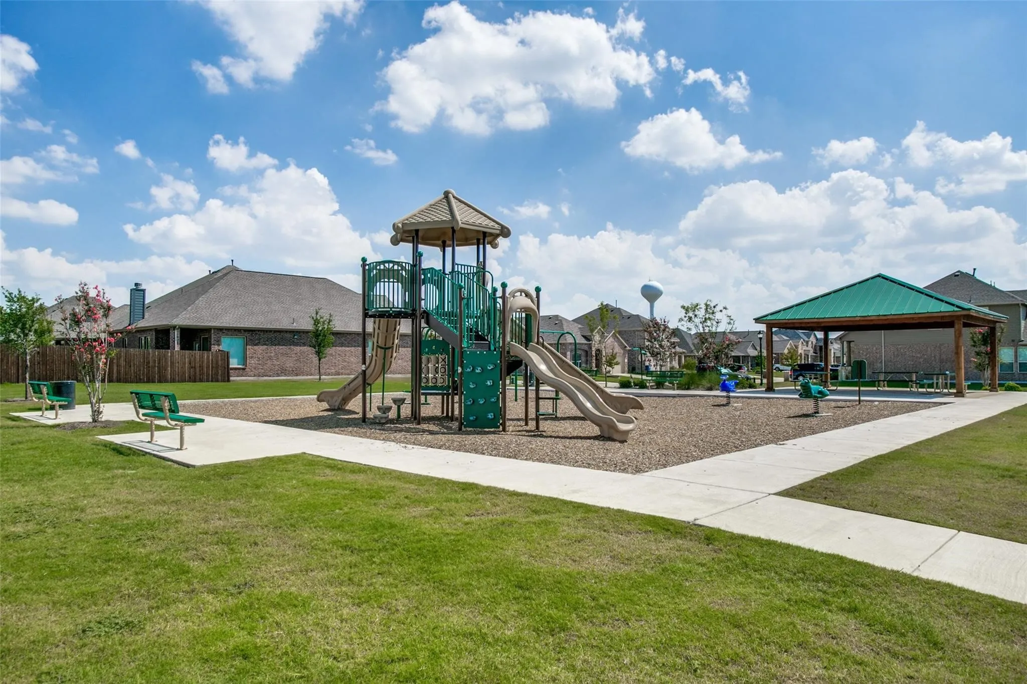 Community playground featuring a multi-level play structure with slides, a covered picnic area, and green benches