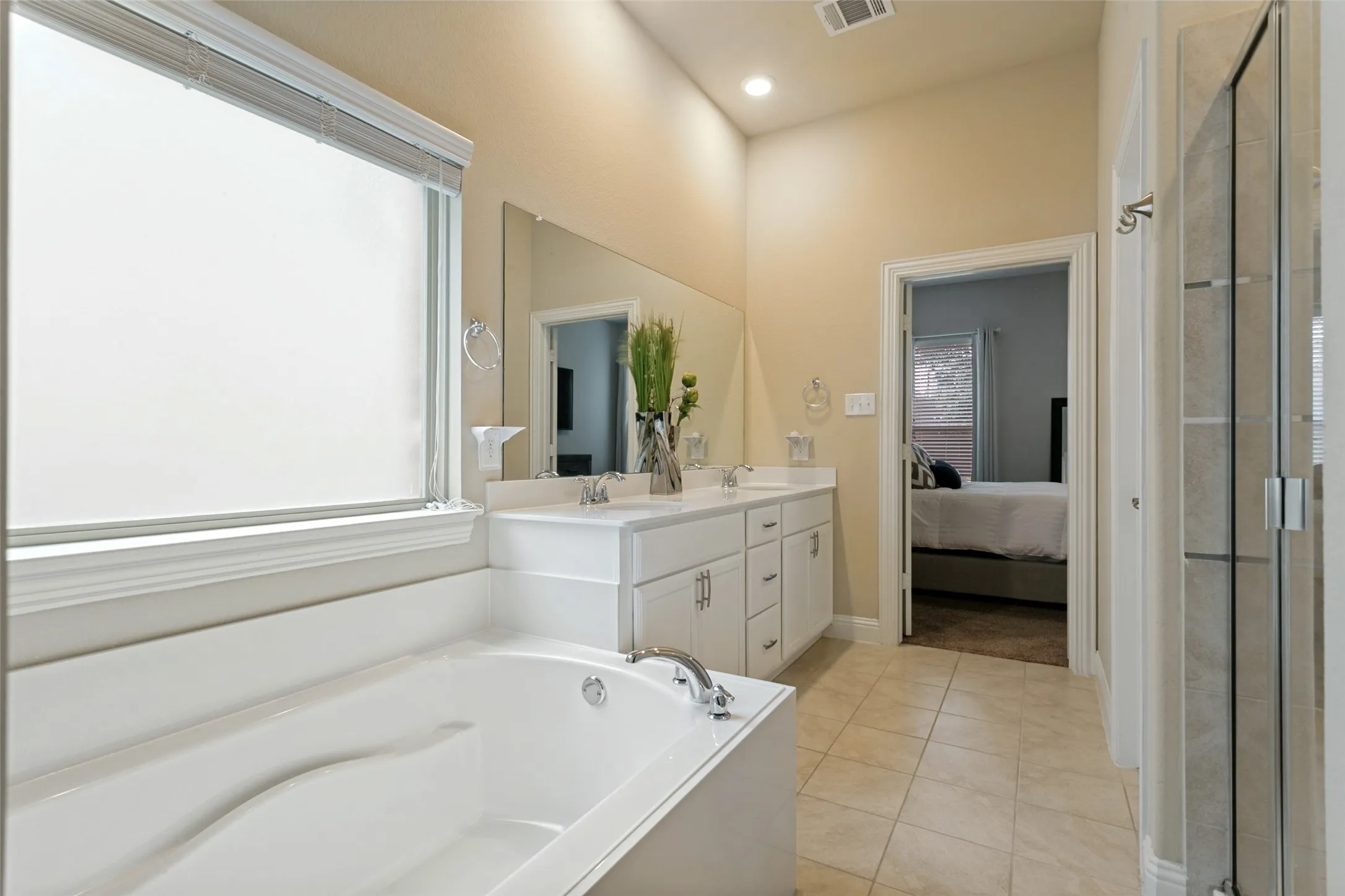 Bathroom featuring a built-in tub, dual sink vanity with white cabinetry, large mirror, and tiled flooring