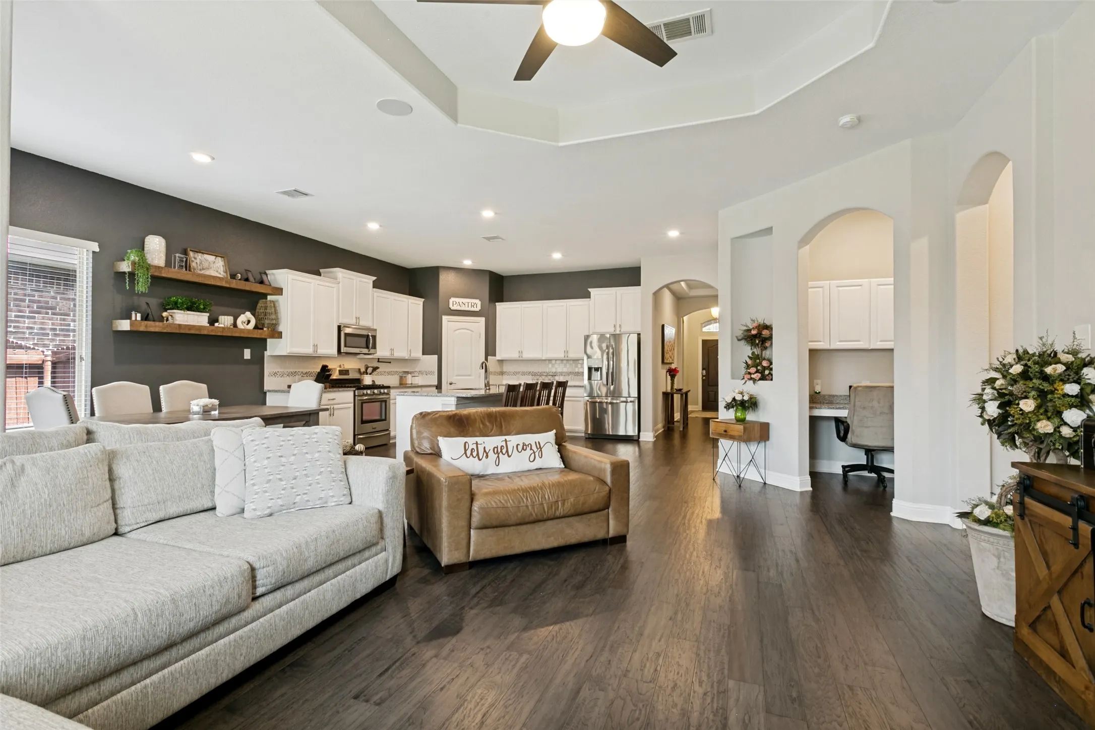 Expansive living space featuring dark wood-finish flooring, a tray ceiling with a ceiling fan, recessed lighting, and a dedicated desk alcove with built-in cabinetry