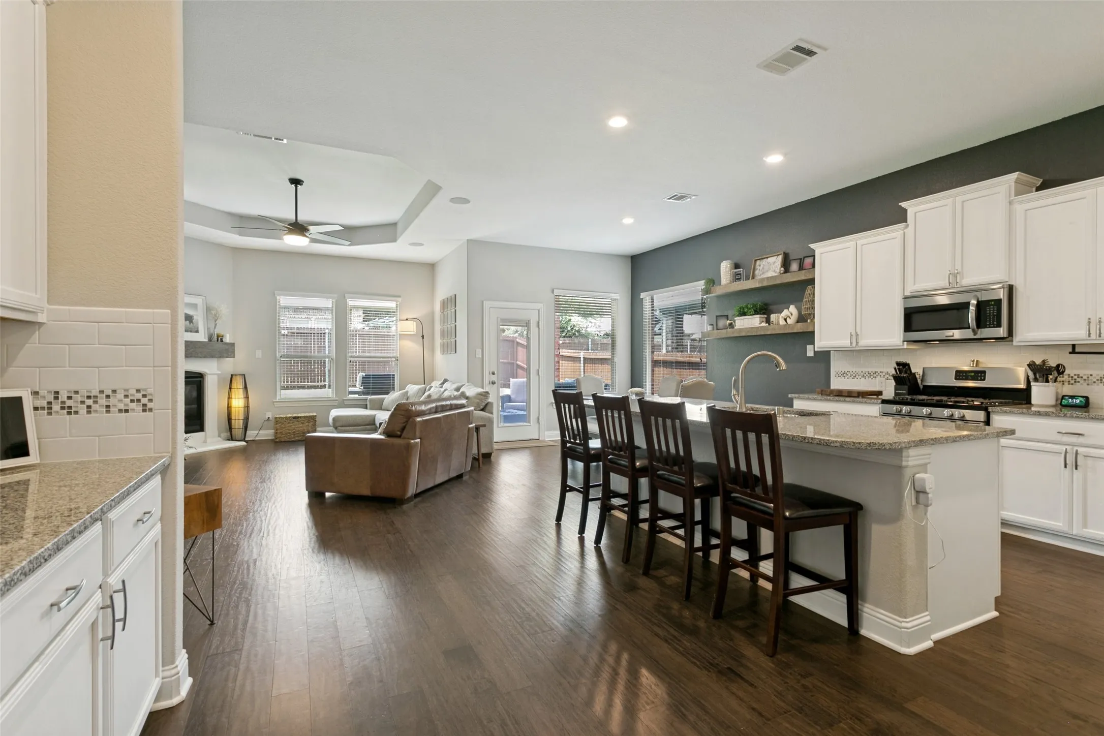 Open-concept living space featuring wood-finish flooring, a kitchen island with seating, white cabinetry, stainless steel appliances, and a tray ceiling in the living area