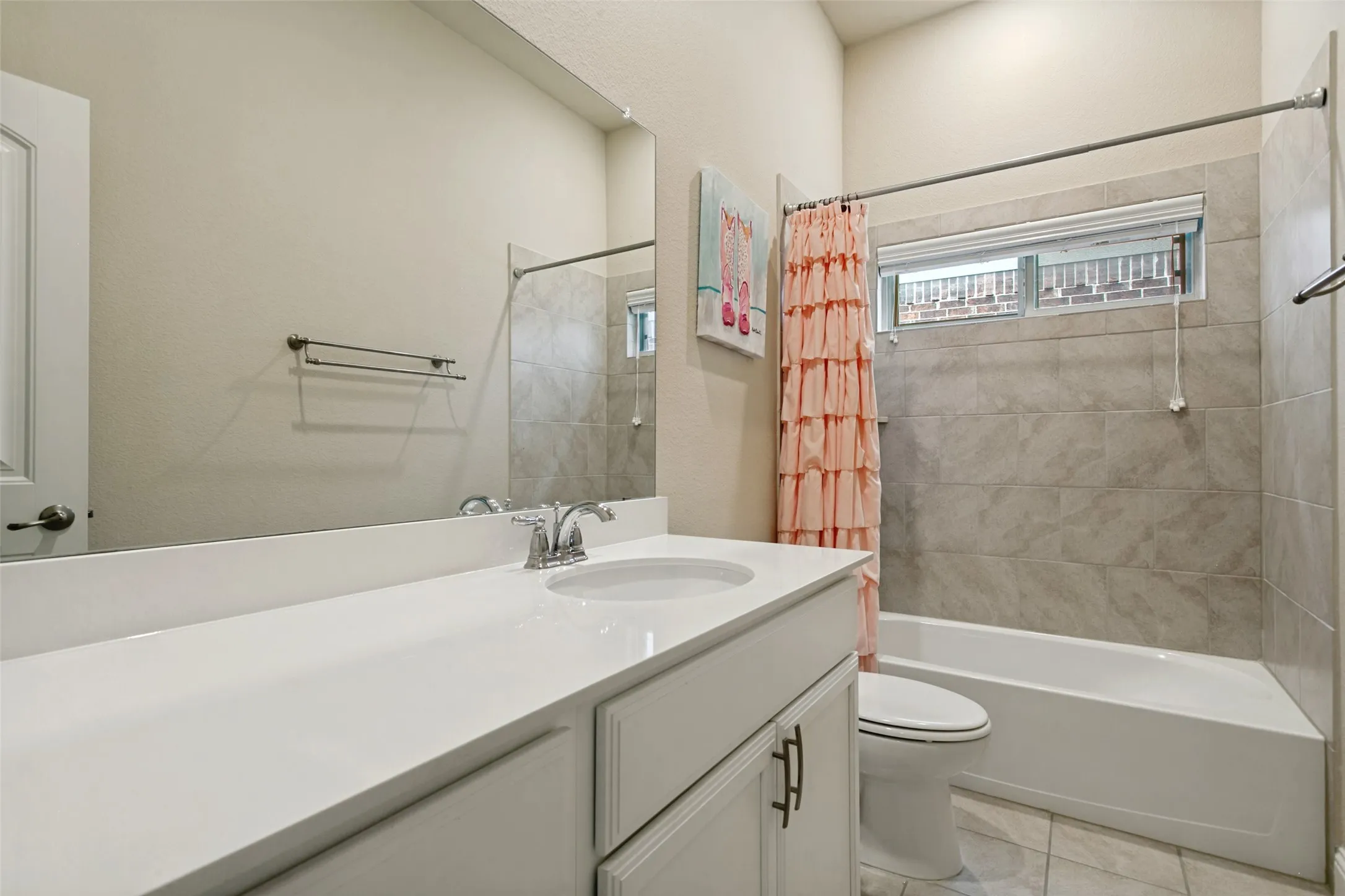 Bathroom featuring a white vanity with an integrated sink and chrome faucet, a large frameless mirror, a white bathtub with tile surround, and a high window