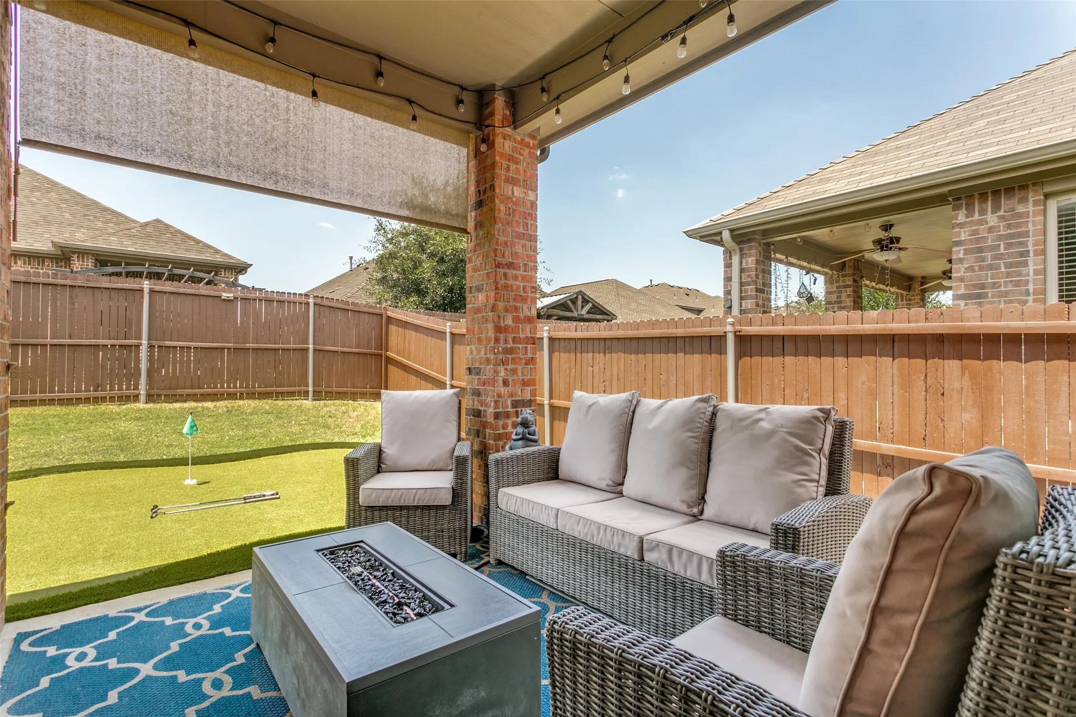 Covered patio featuring a ceiling-mounted shade, brick column, string lighting, and a fire pit table