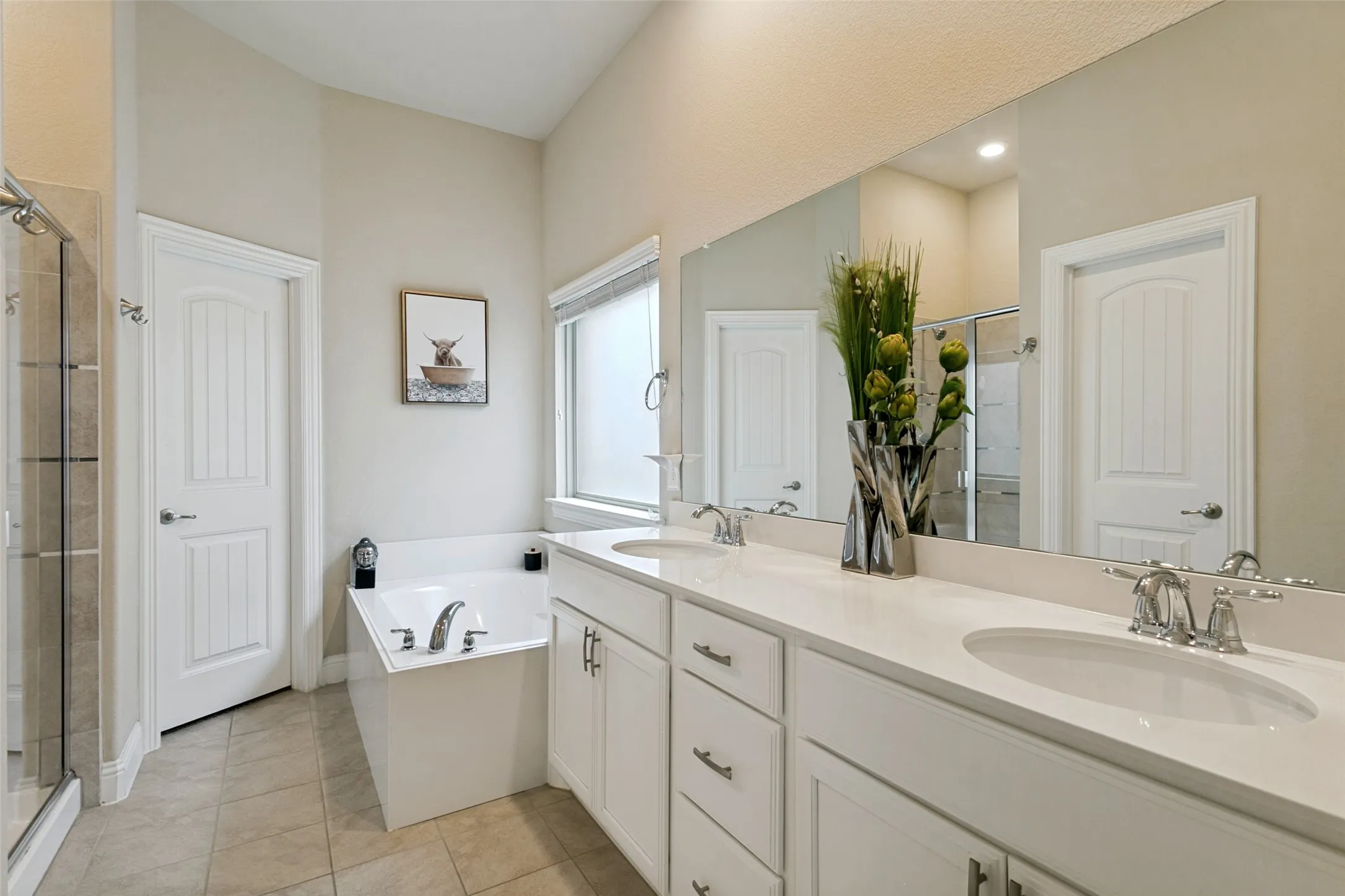 Bathroom featuring a dual vanity with undermount sinks, a large vanity mirror, an enclosed glass shower, a soaking tub, and tile flooring