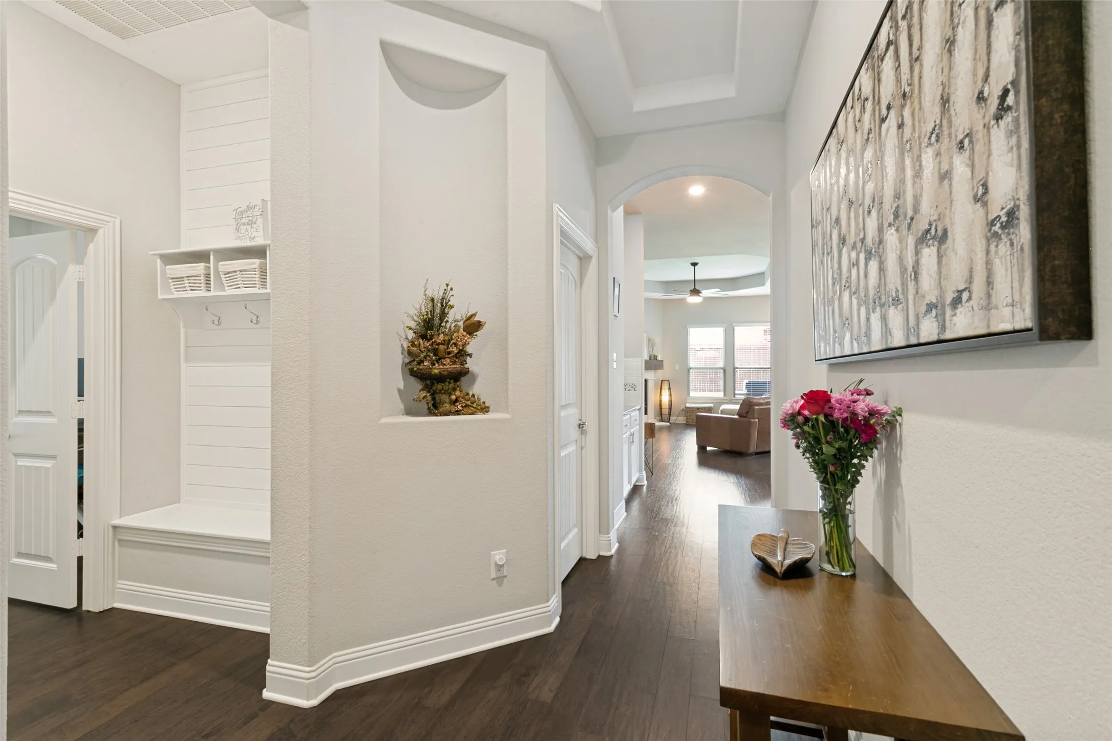 Entryway featuring dark wood-finish flooring, a built-in shiplap bench with storage, a wall niche, an arched doorway, and tray ceilings