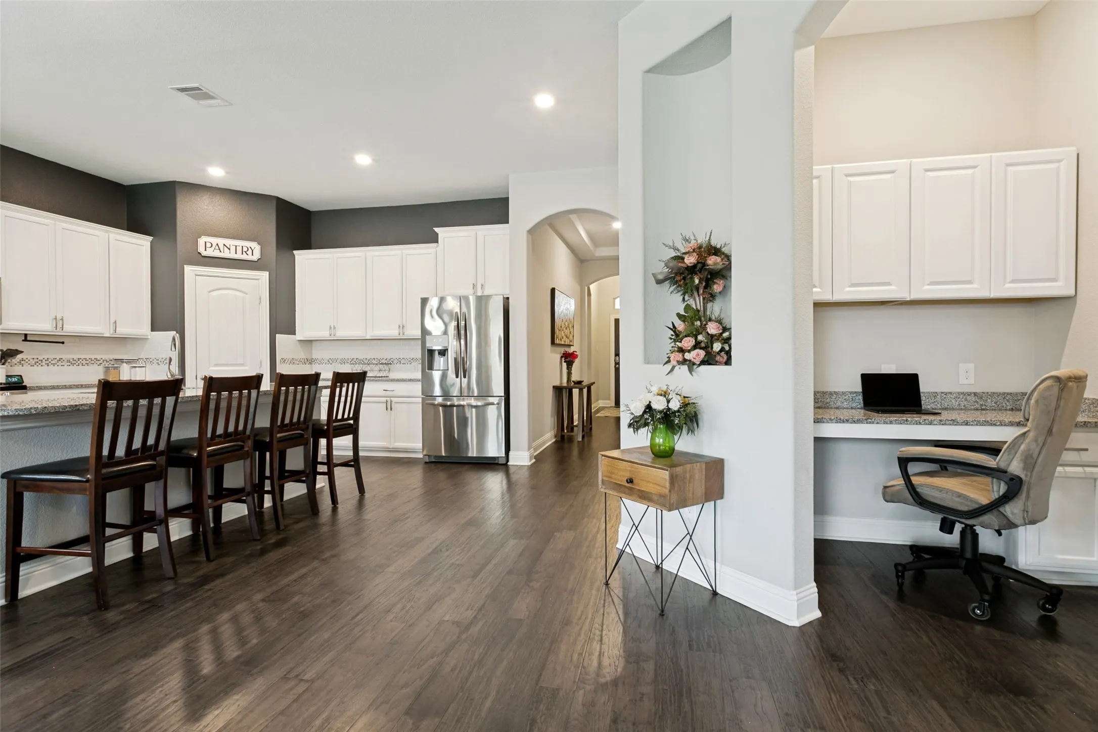 Expansive kitchen featuring white cabinetry, light-toned countertops, a stainless steel refrigerator, and wood-finish flooring