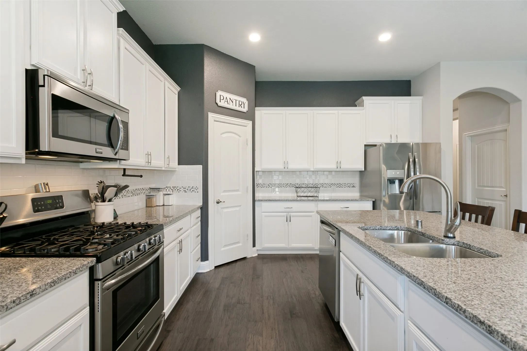 Modern kitchen featuring white cabinetry, stainless steel appliances, speckled stone countertops, and wood-finish flooring