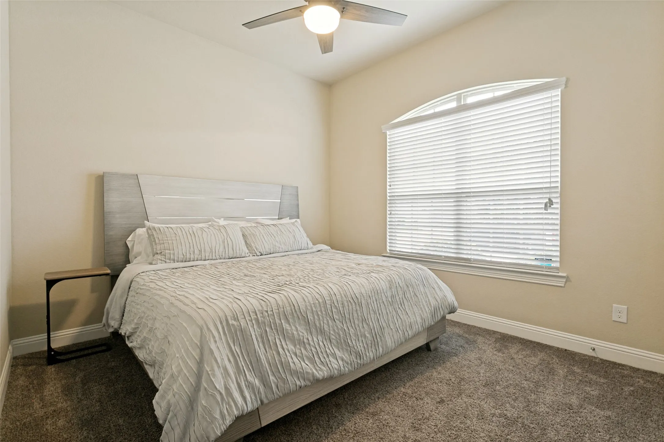 Carpeted room featuring an arched window with blinds, a ceiling fan with integrated lighting, and vaulted ceilings