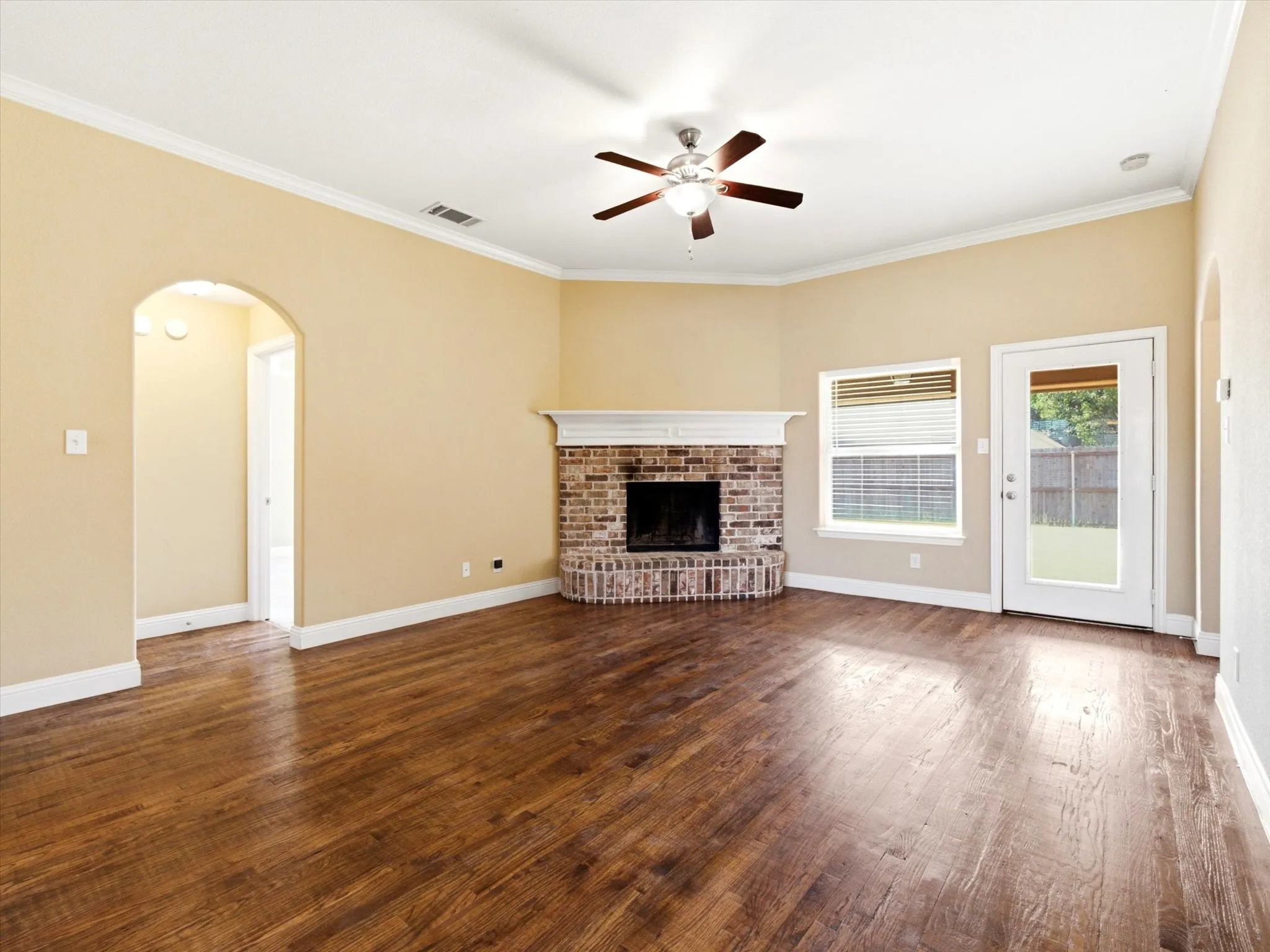 Spacious living area showcasing rich wood-finish flooring, warm neutral walls, and a ceiling fan with brushed nickel finish