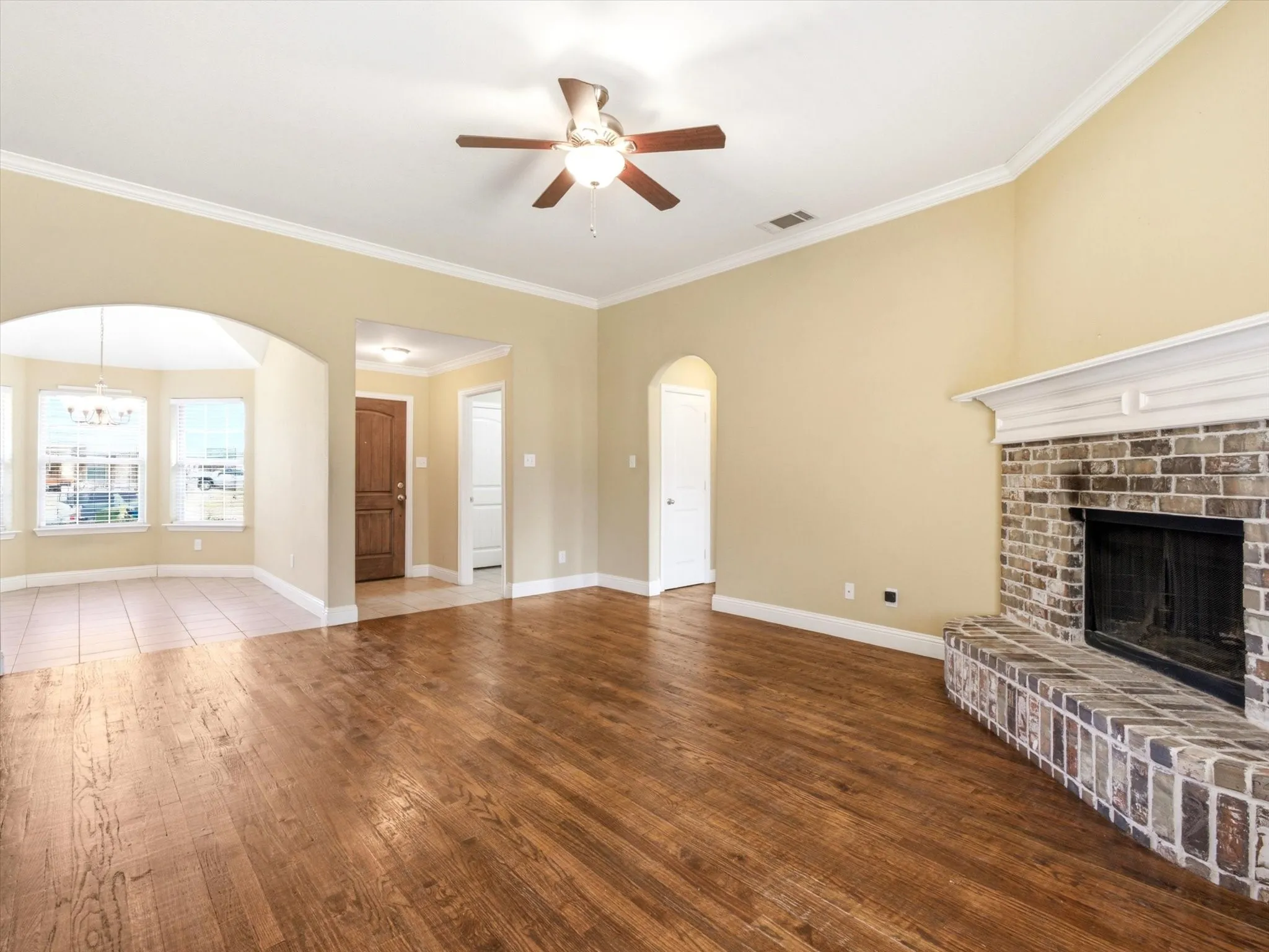 Living area featuring wood-finish flooring, a brick-surround fireplace with a white mantel, and a ceiling fan with integrated lighting