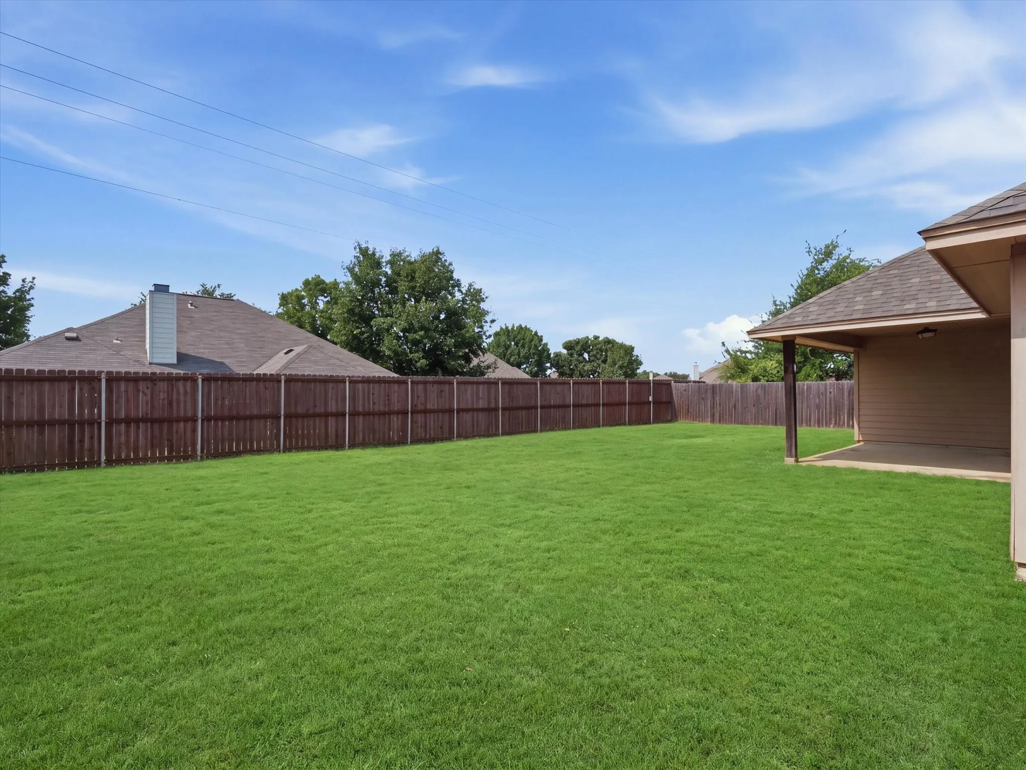 Expansive backyard featuring a lush lawn, privacy fencing, and a covered patio