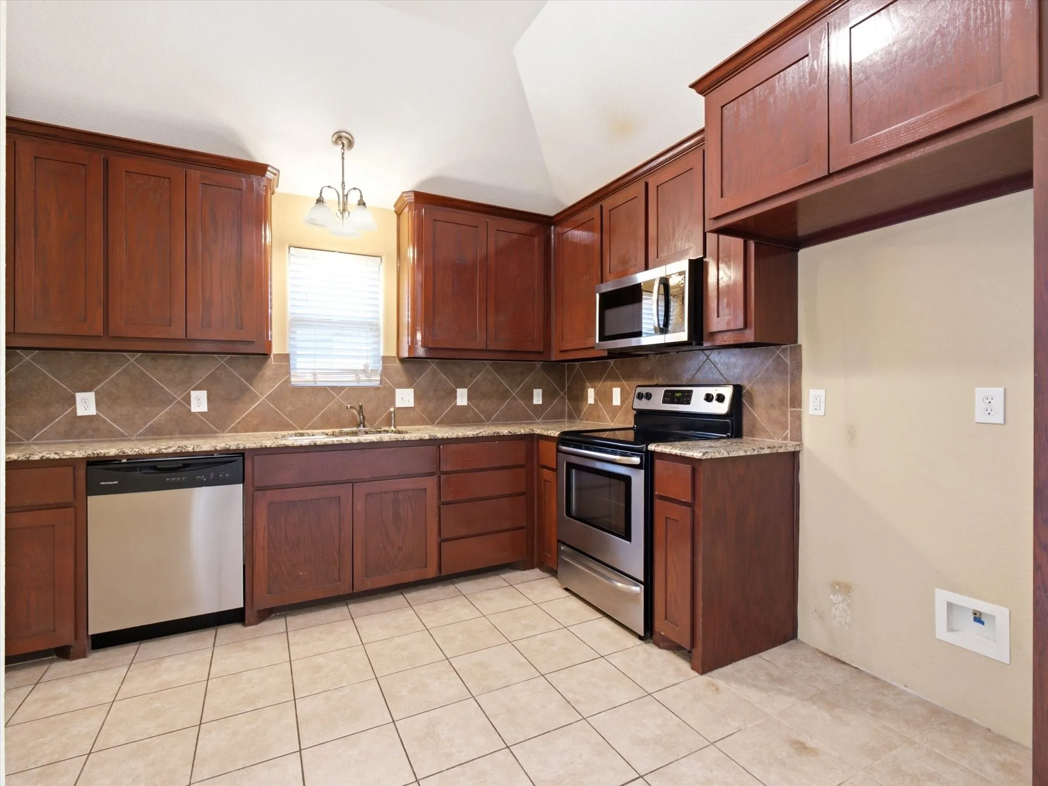 Spacious kitchen featuring rich wood cabinetry throughout, stainless steel appliances including a slide-in range and microwave, tile backsplash, tile flooring, and ample counter workspace