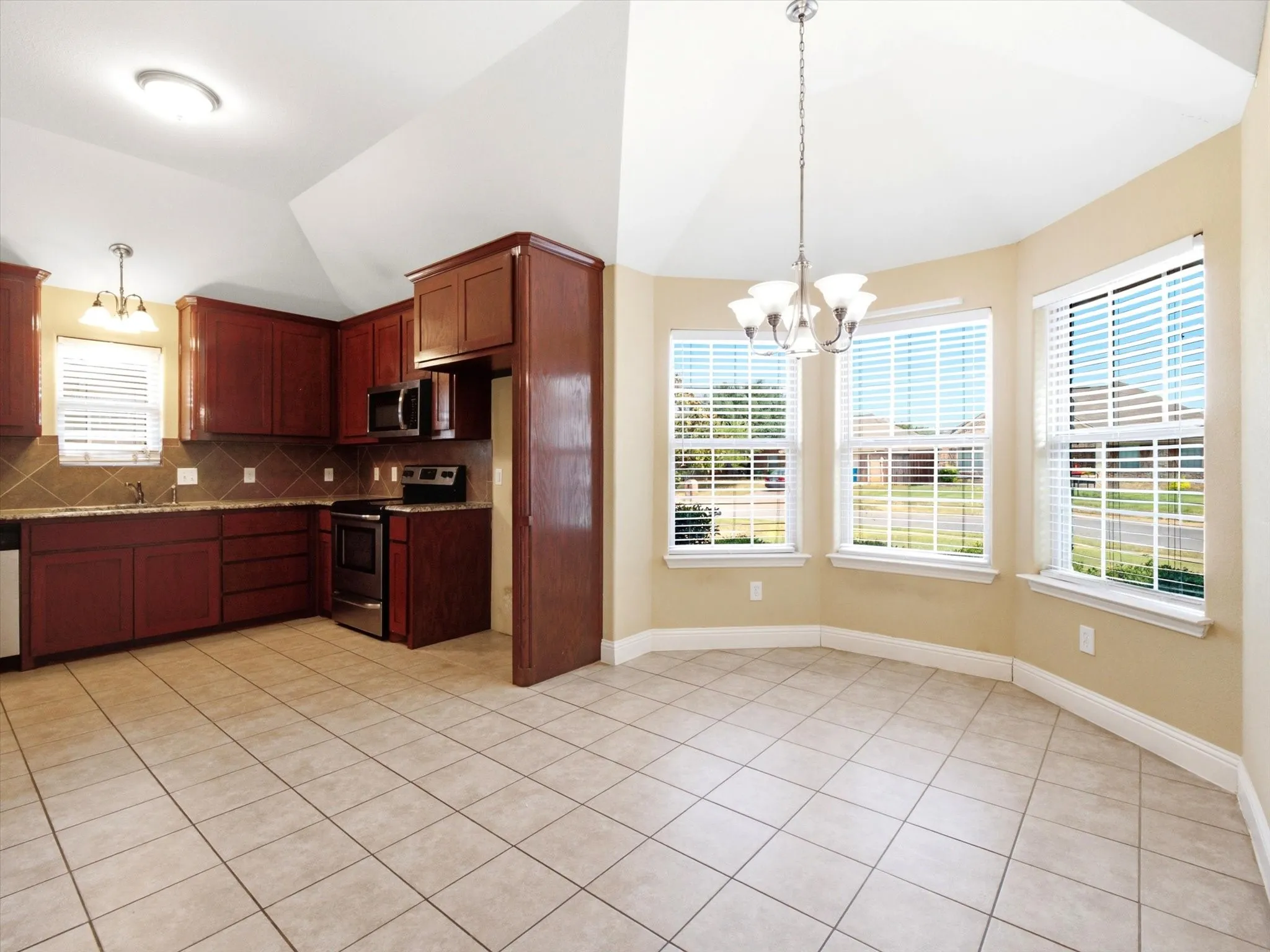 Kitchen and dining area featuring tile flooring, vaulted ceiling, bay windows, wood cabinetry, and stainless-steel appliances