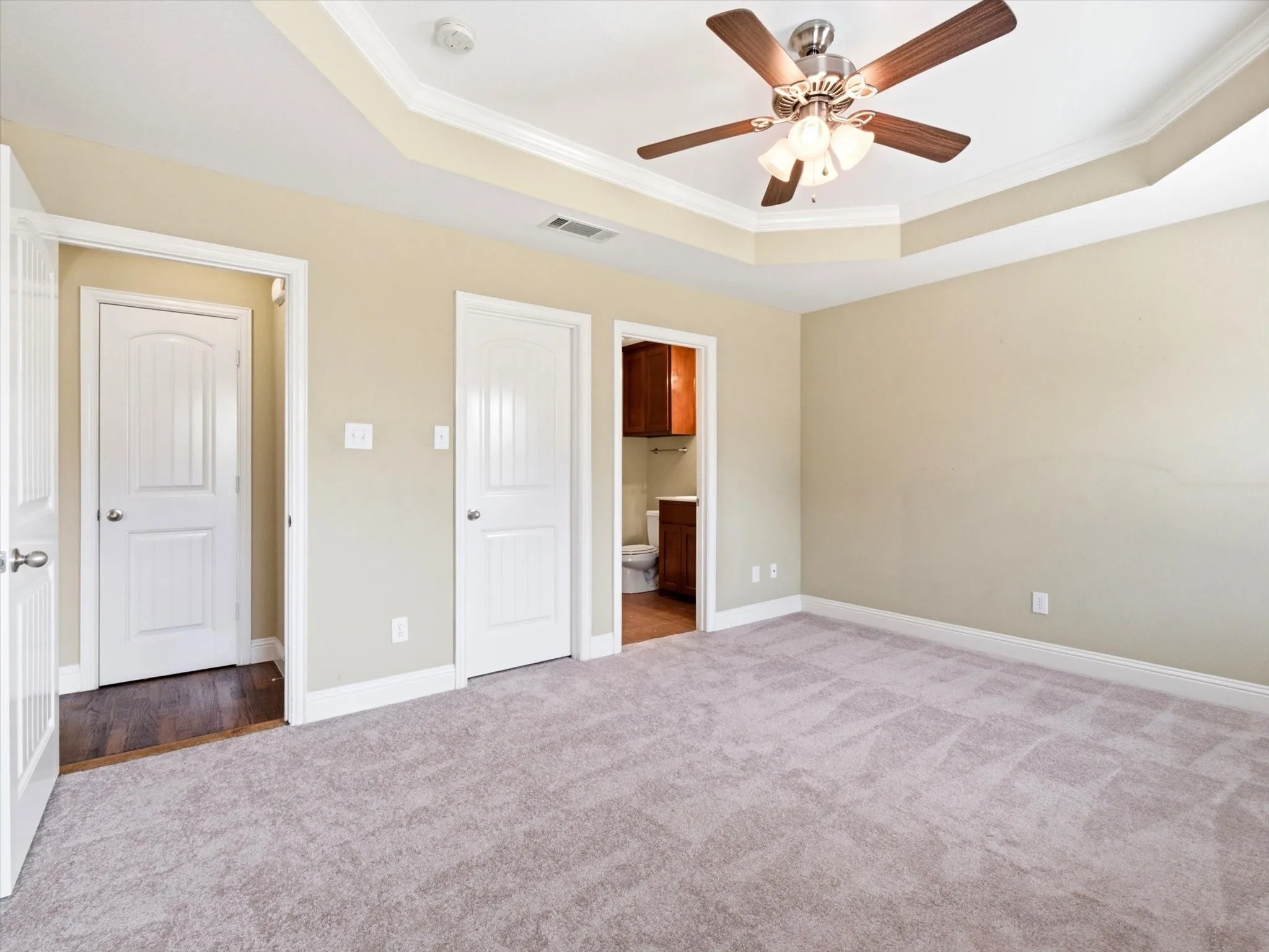 Spacious room featuring tray ceilings with crown molding, ceiling fan with light fixture, light gray carpeting, and neutral wall tones