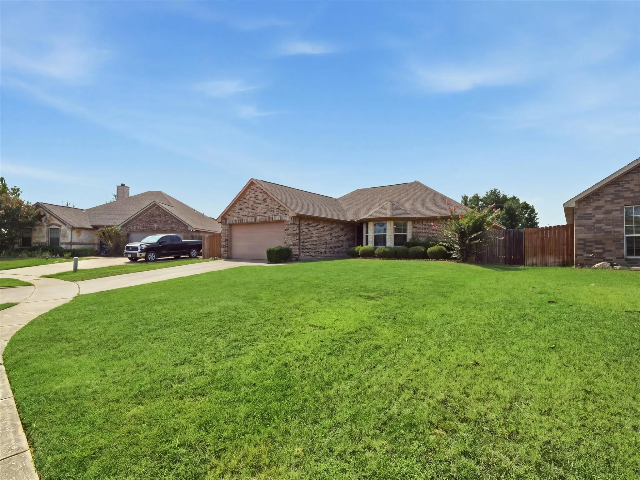 Charming brick residence featuring a spacious manicured lawn, mature landscaping with established trees, and a welcoming architectural design with multiple gabled rooflines