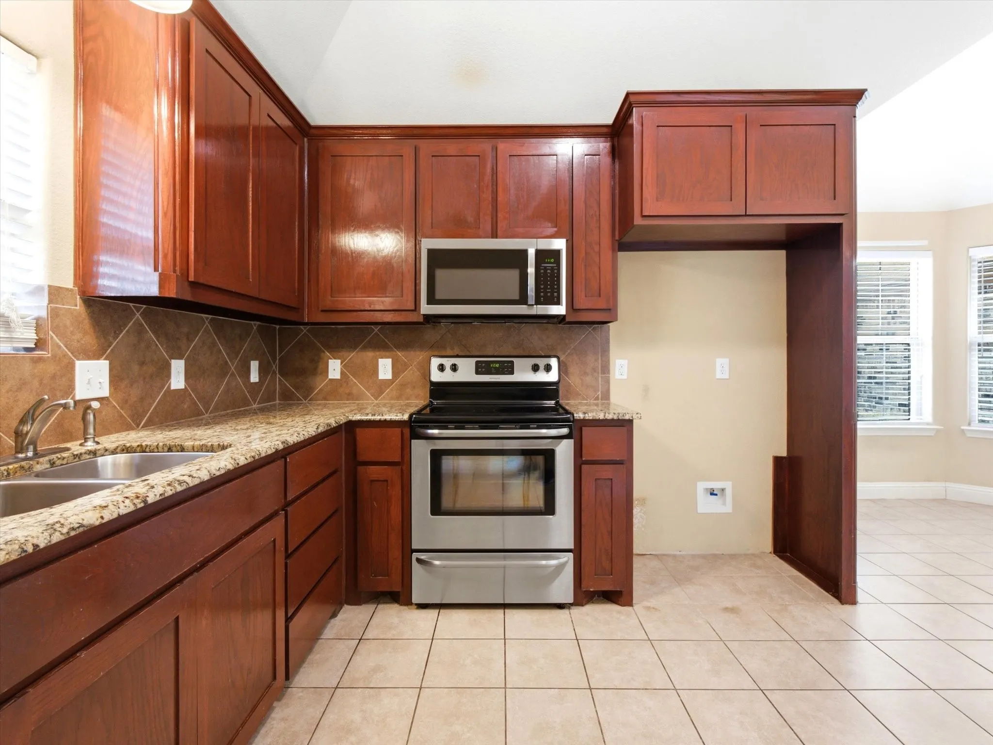 Warm wood cabinetry with stainless steel appliances and a tile backsplash define this kitchen space